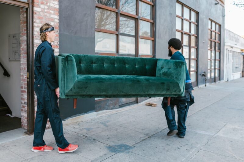 two movers holding a green couch on street
