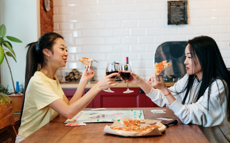 two people eating pizza and clinking wine glasses at a restaurant