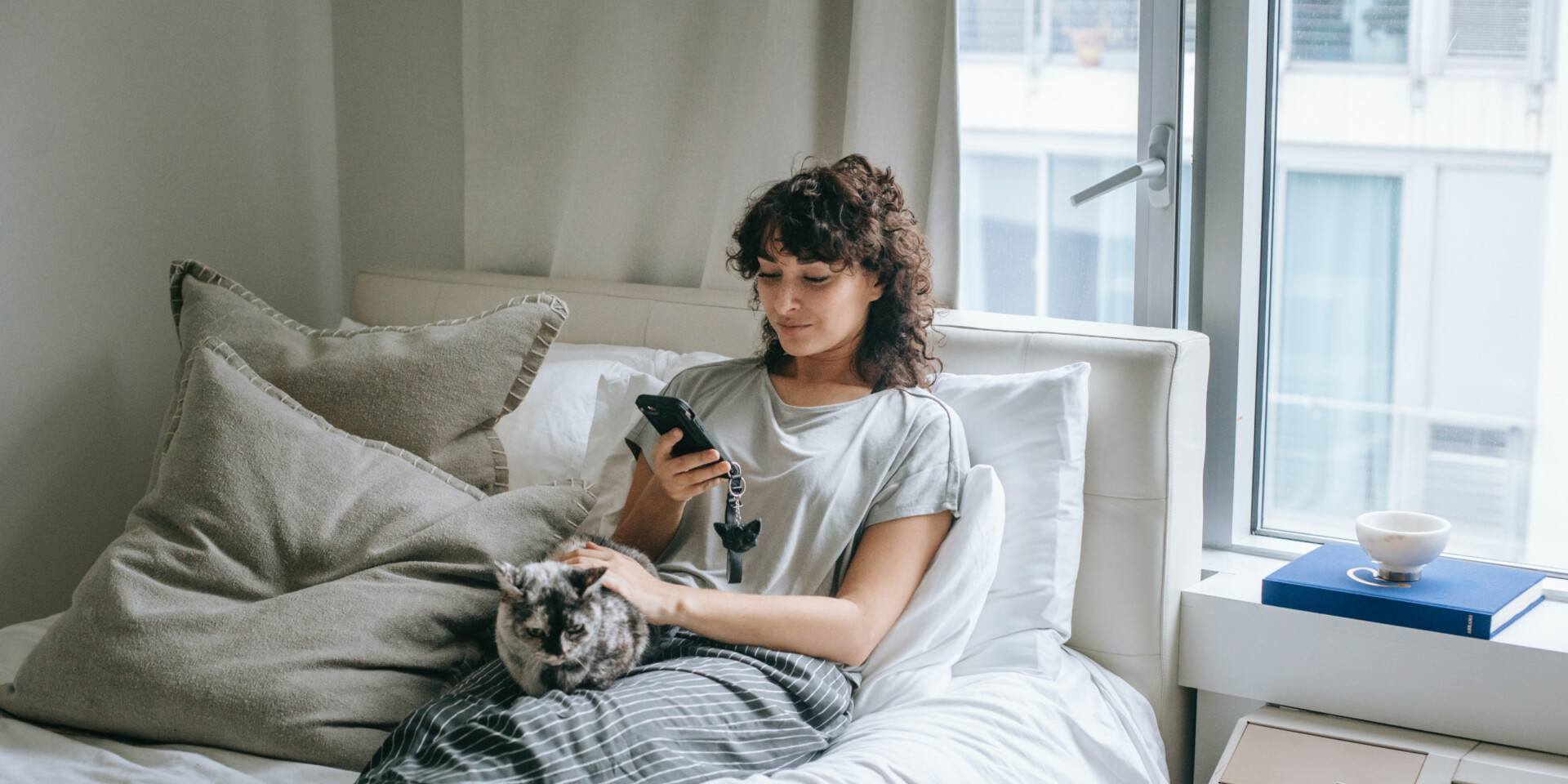 woman scrolling on phone in her apartment sitting next to her cat