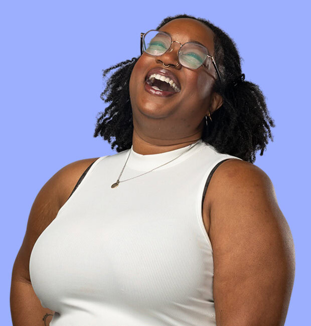 A person with curly, shoulder-length hair is laughing joyfully. They are wearing a sleeveless white top and a delicate necklace. The background is a soft lavender color, enhancing the cheerful expression. The overall mood of the image is vibrant and positive.