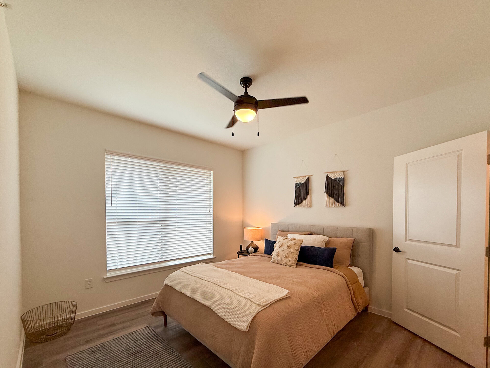 A cozy bedroom features a large window with blinds, enhancing the room's inviting atmosphere with natural lighting. A white door is partially open, leading to a closet.