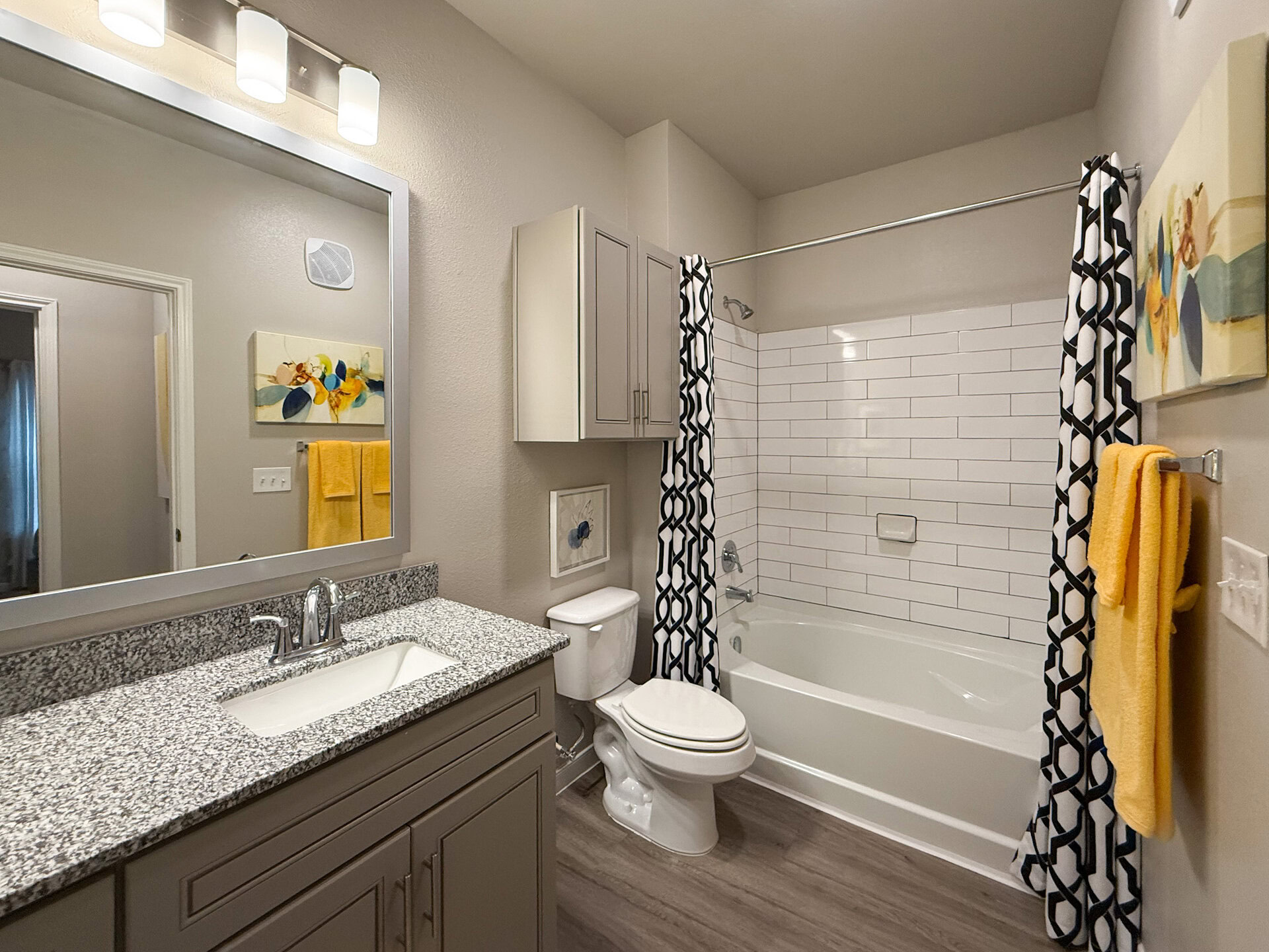 A modern bathroom featuring a white bathtub with a shower, surrounded by white subway tiles. The space includes a granite countertop with a sink and a stylish faucet.