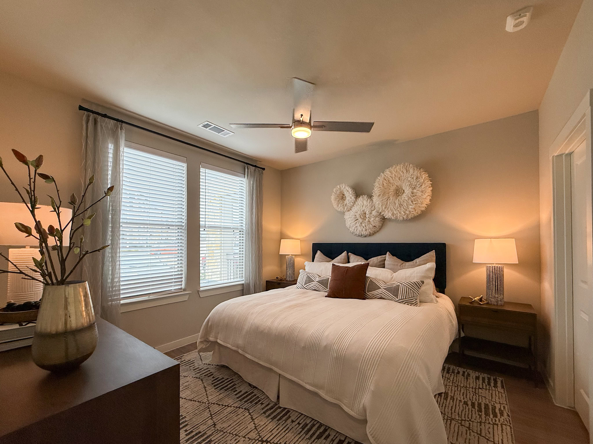 A cozy bedroom features a large bed with large windows. Natural light streams in through two large windows and an upgraded ceiling fan.