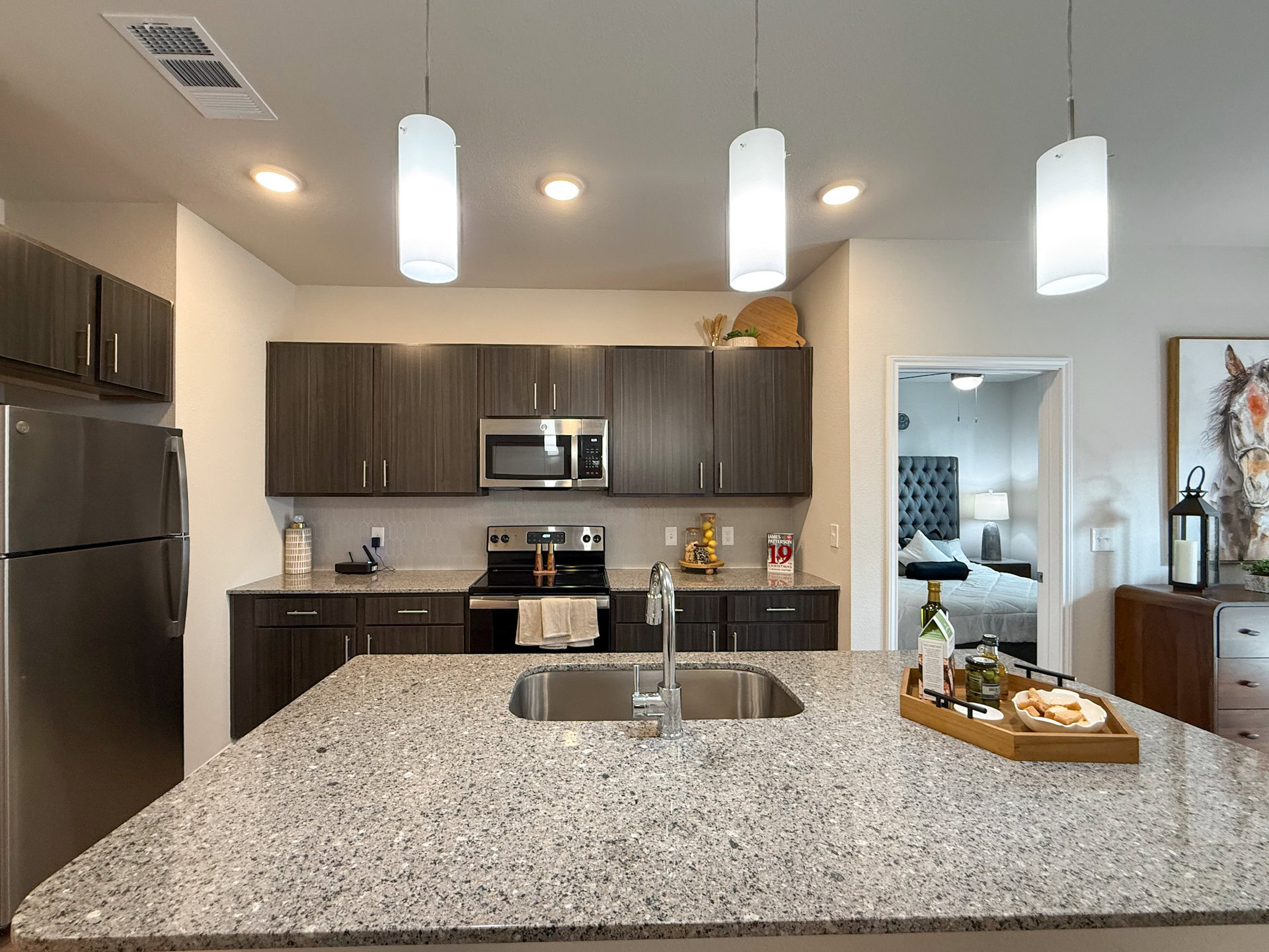 A modern kitchen features dark wood cabinetry and a granite countertop. Stainless steel appliances, including a refrigerator and an oven. A farmhouse sink with a sleek faucet is integrated into the countertop.