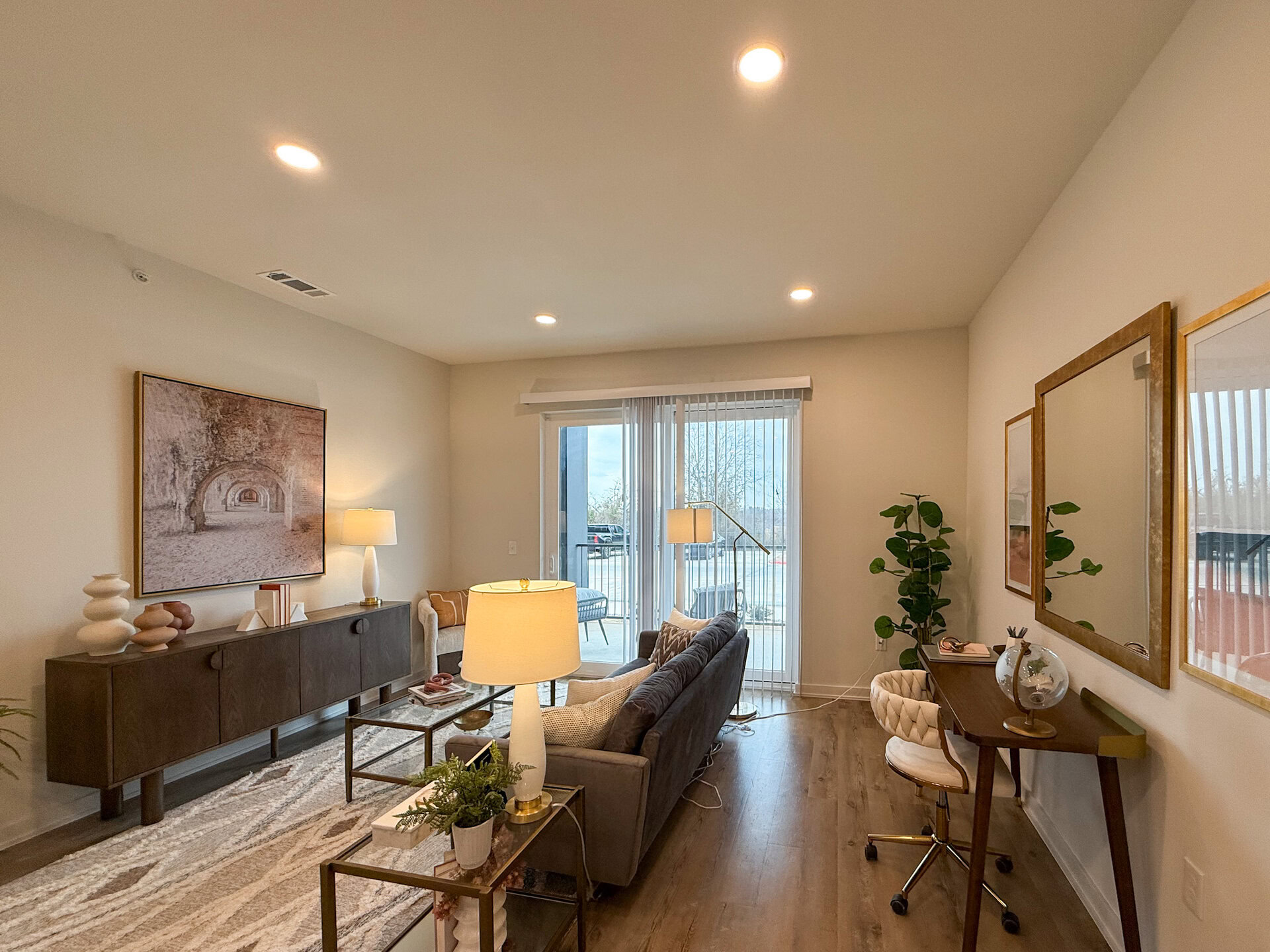 A cozy living room features natural light streaming in through sliding glass doors, which lead to an outdoor area. The flooring is a warm wood tone, enhancing the inviting atmosphere.