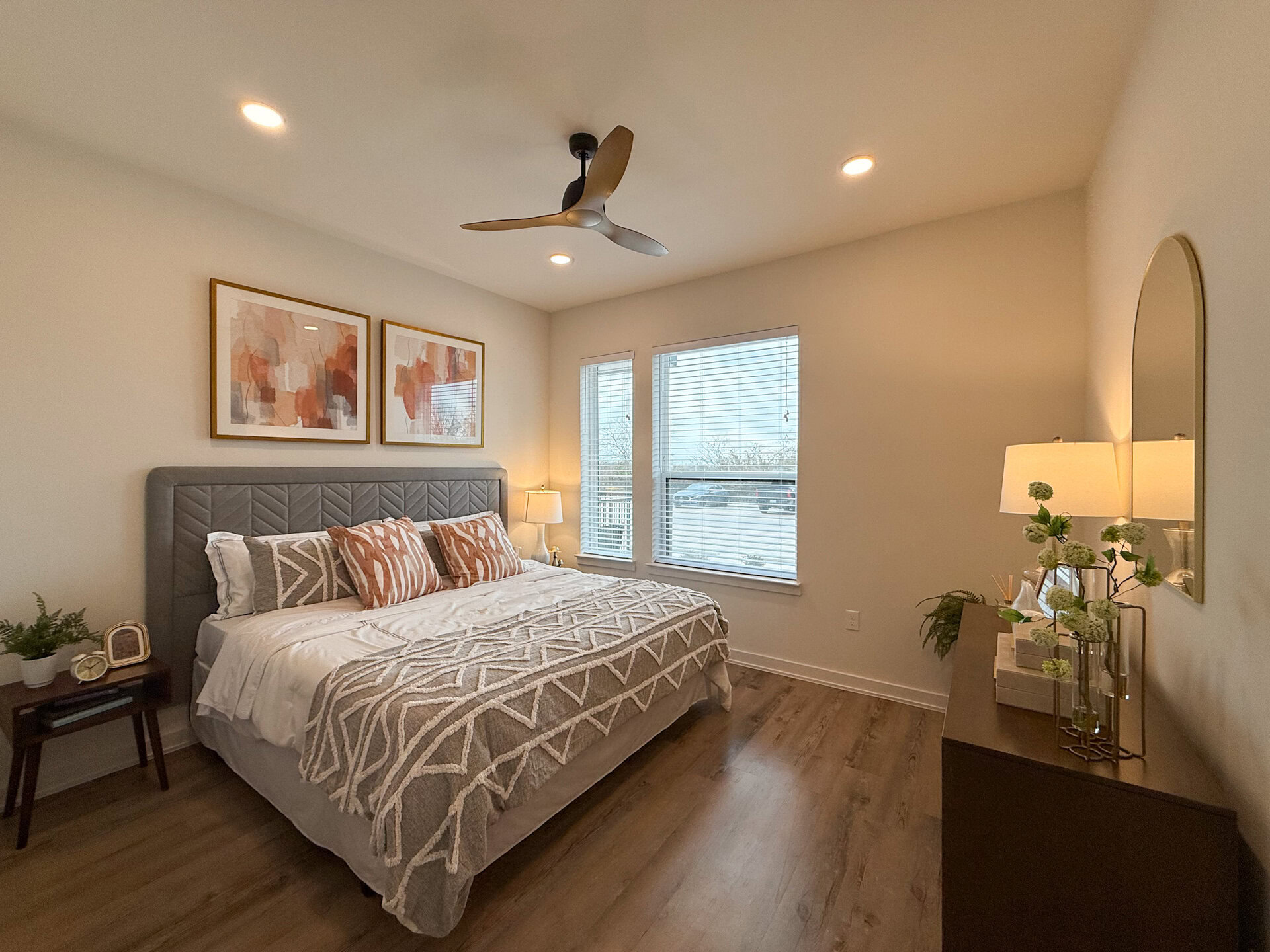 A cozy bedroom features a queen-sized bed. The flooring is a warm wood tone, enhancing the inviting atmosphere. The fan gives the modern luxe feeling to the room.