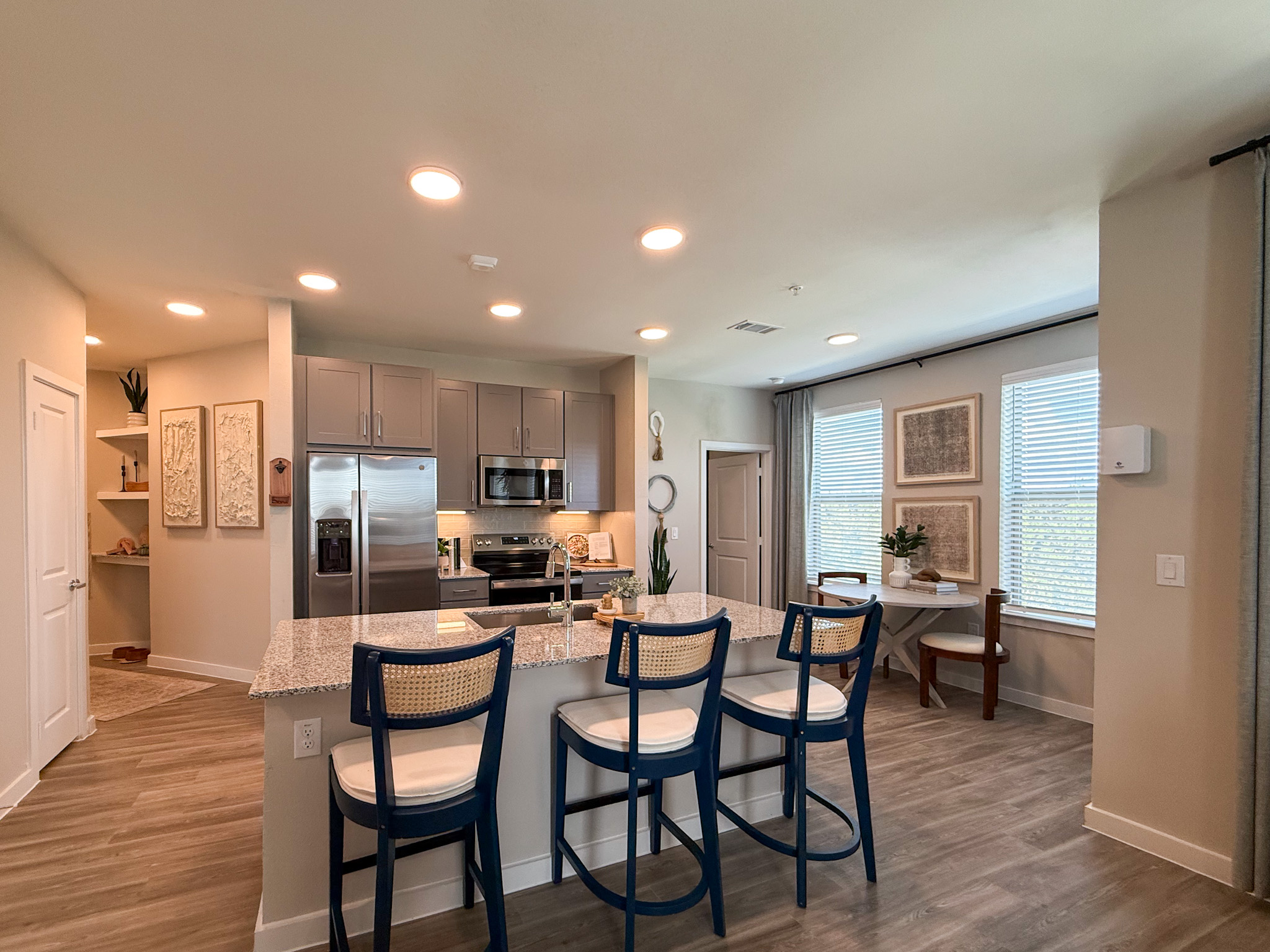 A San Antonio modern apartment kitchen features sleek gray cabinets, stainless steel appliances, and a granite countertop with bar seating. The flooring is a light wood finish, enhancing the contemporary feel.