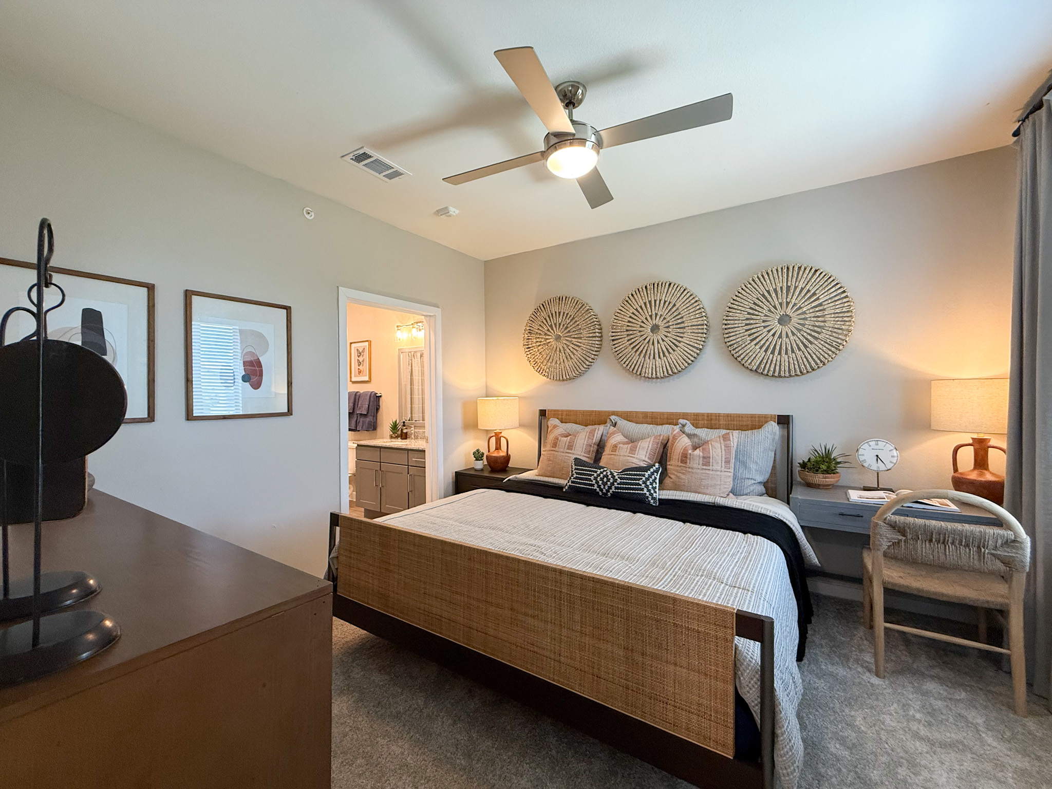 A cozy San Antonio apartment bedroom features a large bed The room is well-lit, with a sleek ceiling fan providing a modern touch.