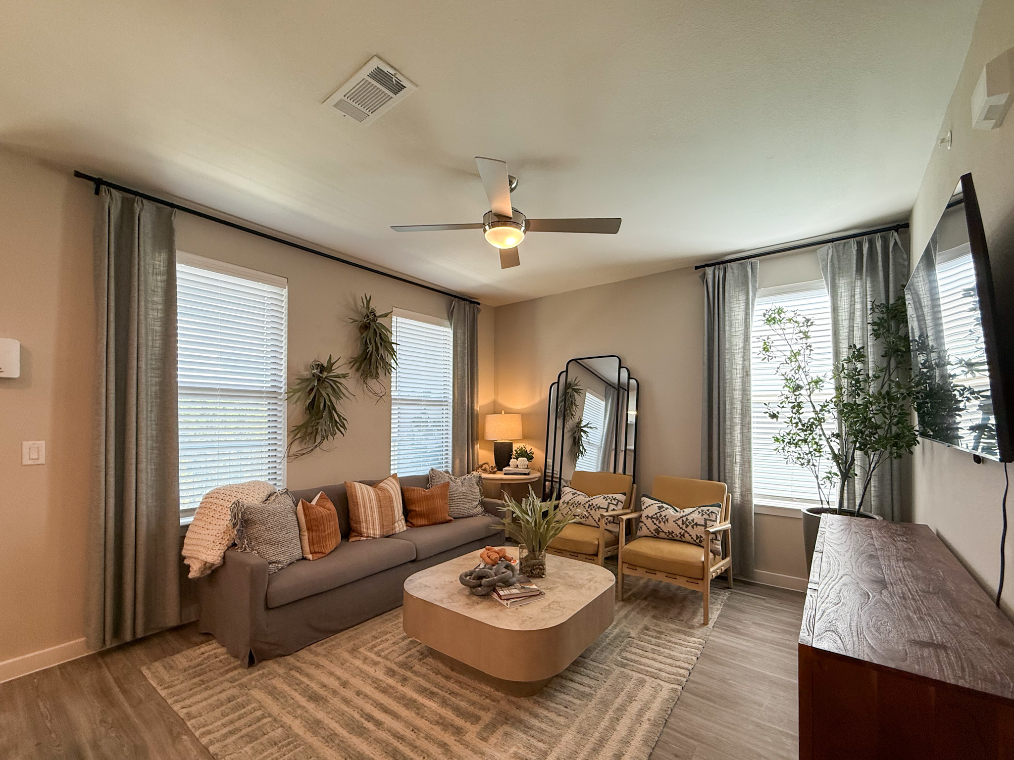 A cozy San Antonio apartment living room. The room is brightened by natural light streaming through two windows. A sleek ceiling fan provides a contemporary touch.