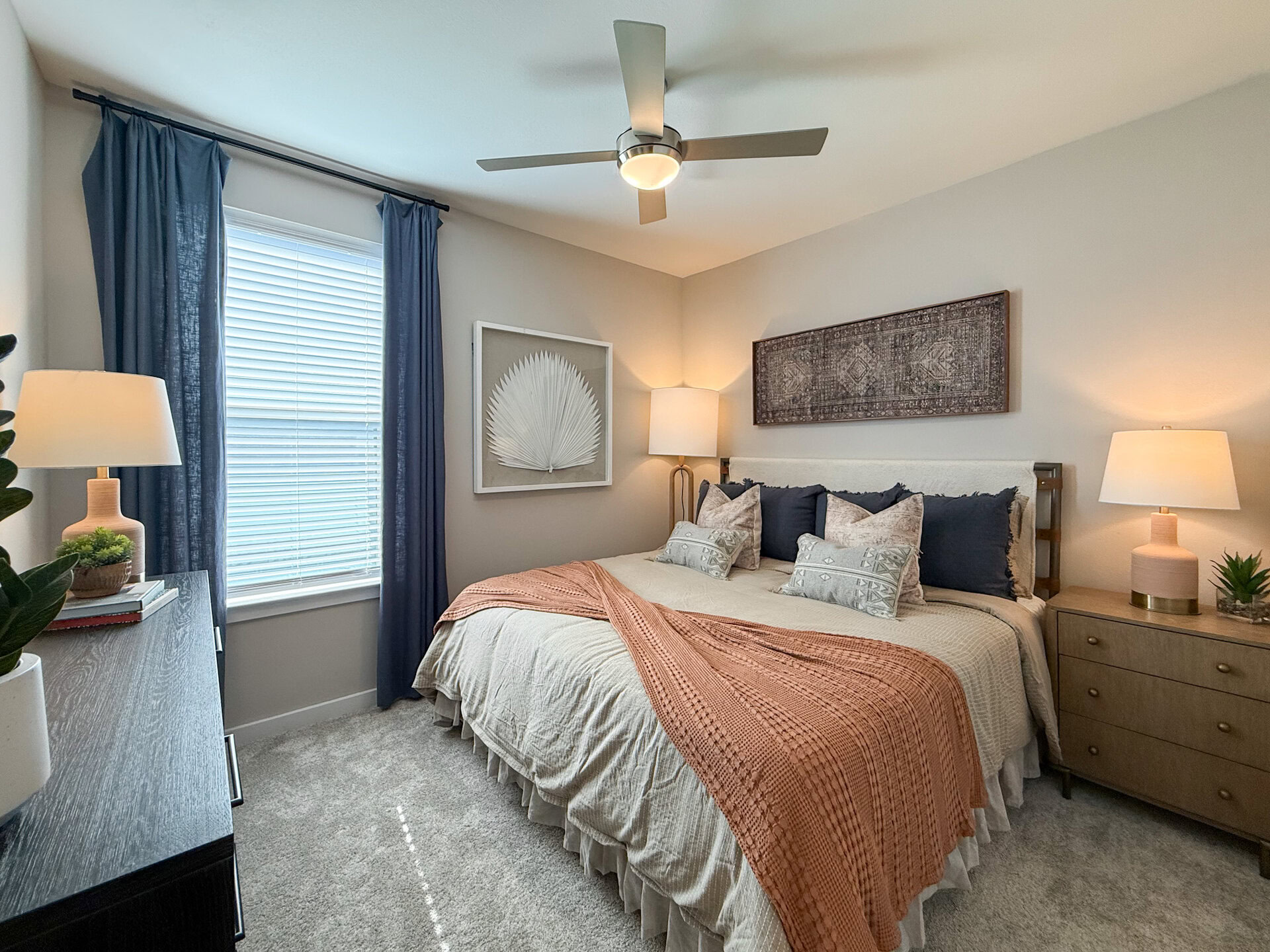 A cozy San Antonio apartment bedroom features a large bed The room is well-lit, with a sleek ceiling fan providing a modern touch.