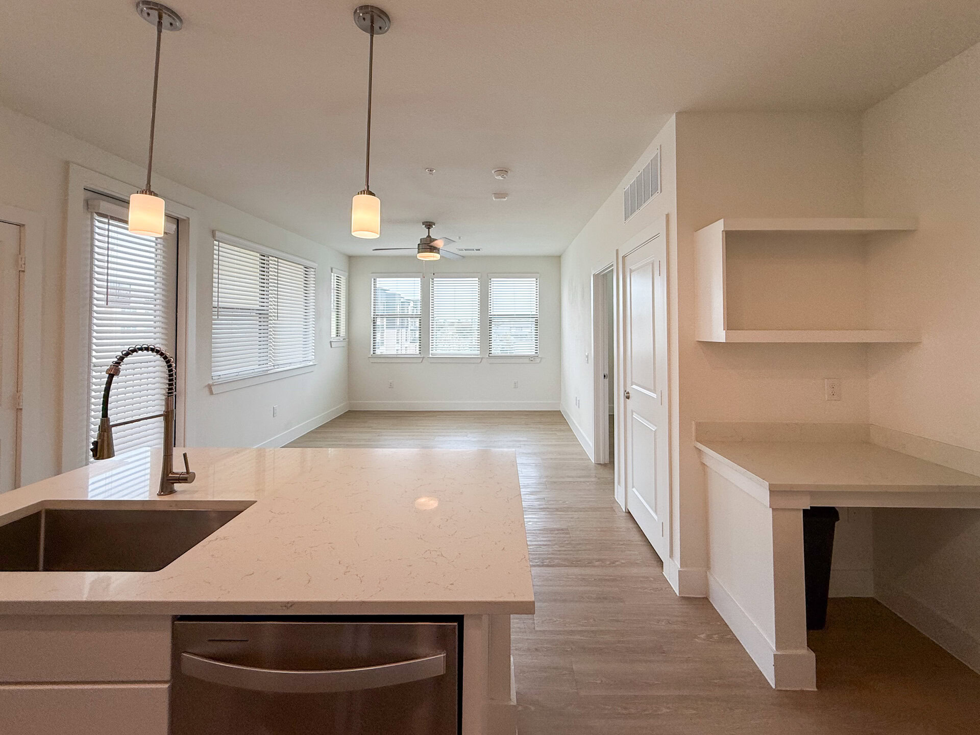 A modern San Antonio apartment living area, featuring light wood flooring, is filled with natural light from multiple windows on both walls. The living room is open with a spacious layout, and the overall color scheme is bright and neutral.