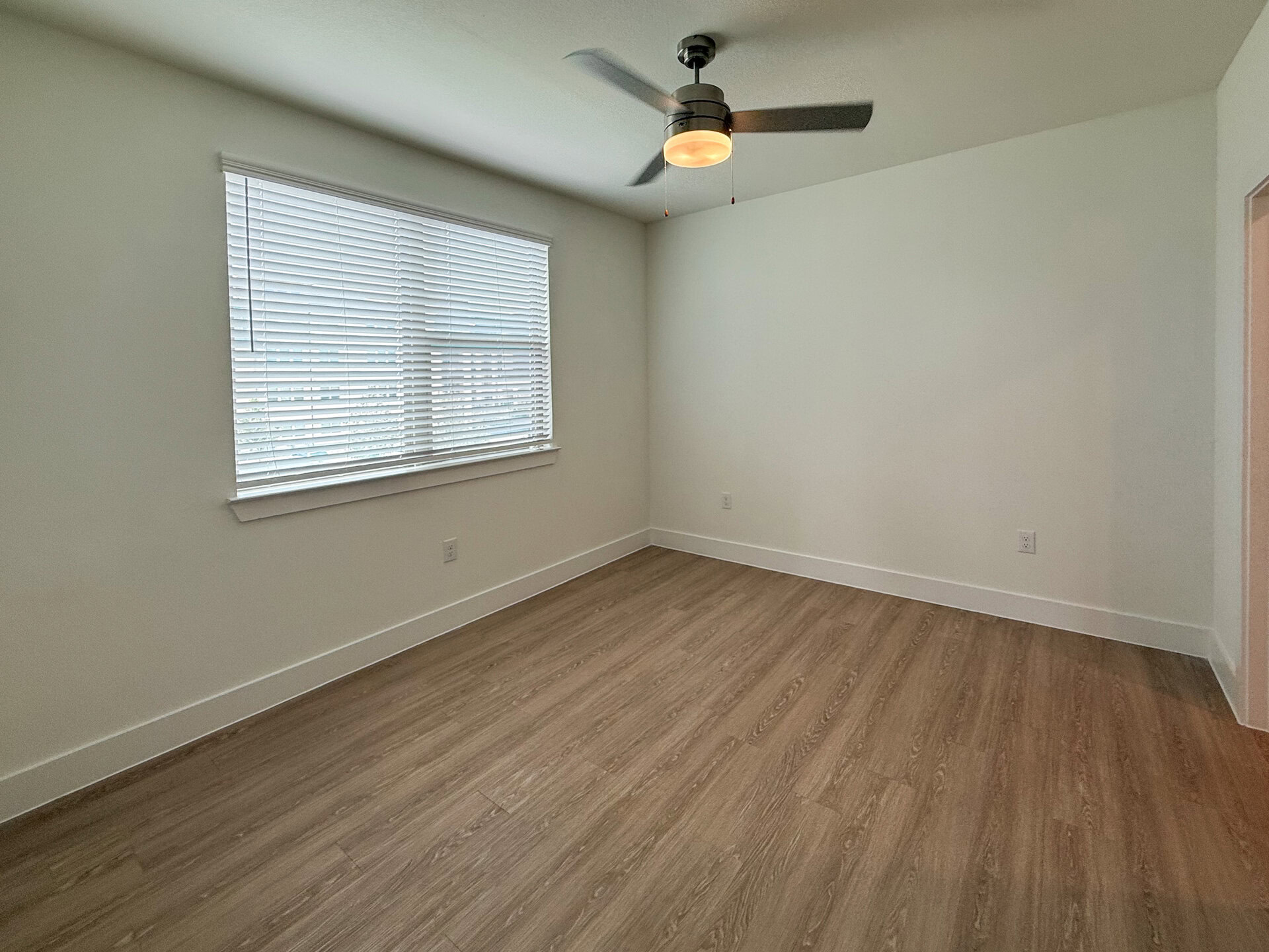 The bright and spacious secondary bedroom features a window with white blinds that allow natural light to enter.