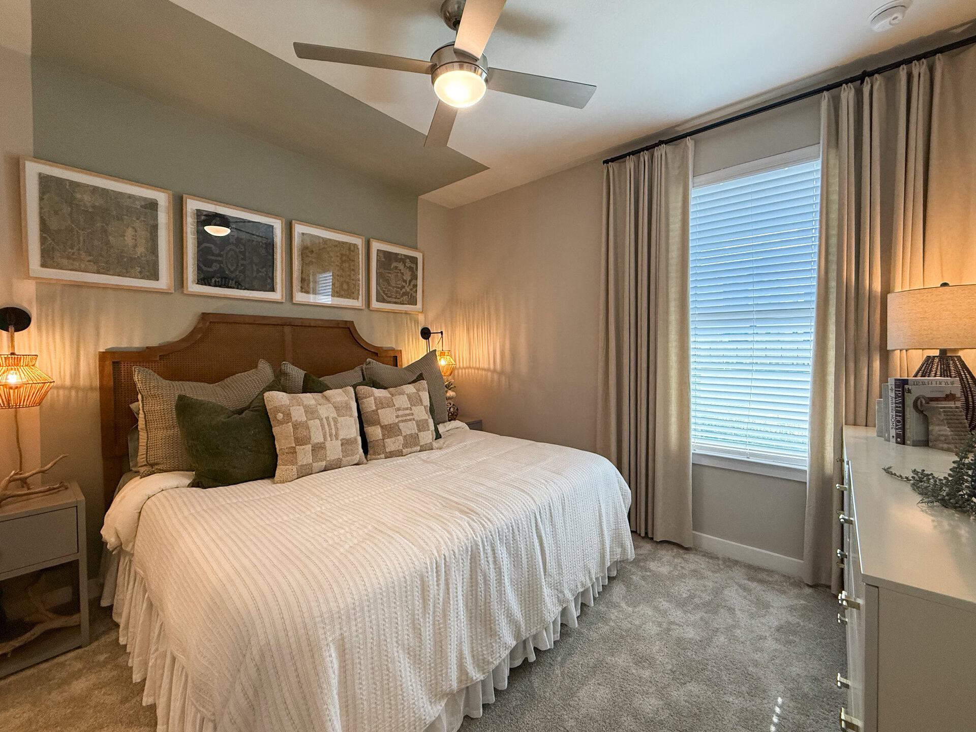A cozy San Antonio apartment bedroom features a window with blinds, allowing natural light to filter in. The room has a calm and inviting atmosphere, enhanced by a light-colored carpet.