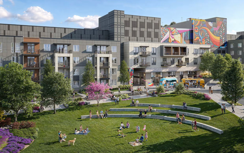 A modern residential complex features multiple stories with a mix of balconies and large windows. In the foreground, a green lawn is dotted with people enjoying leisure activities, some sitting on picnic blankets. There are curved stone benches and vibrant flower beds, including pink flowering trees. Food trucks are visible nearby, and colorful murals adorn the building's exterior, adding a lively atmosphere to the scene. The sky is partly cloudy, enhancing the inviting ambiance.