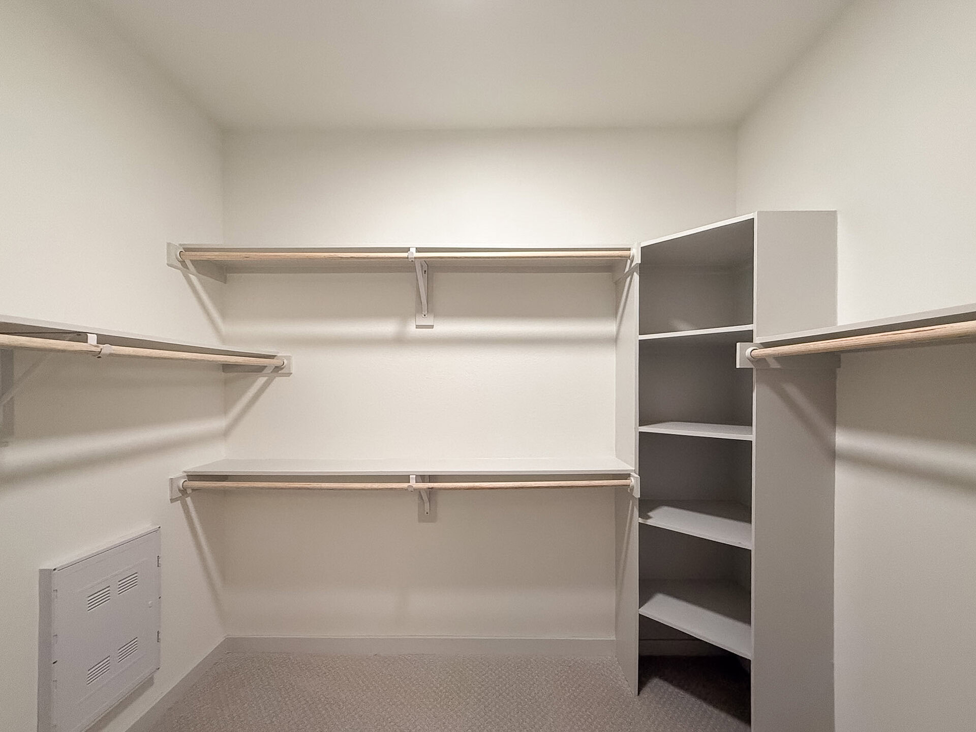 A San Antonio apartment's spacious closet features a combination of wooden and gray shelving. There are two horizontal wooden rods for hanging clothes, positioned at different heights. On the right side, a gray shelving unit with multiple open compartments provides additional storage space. The overall design is clean and modern.